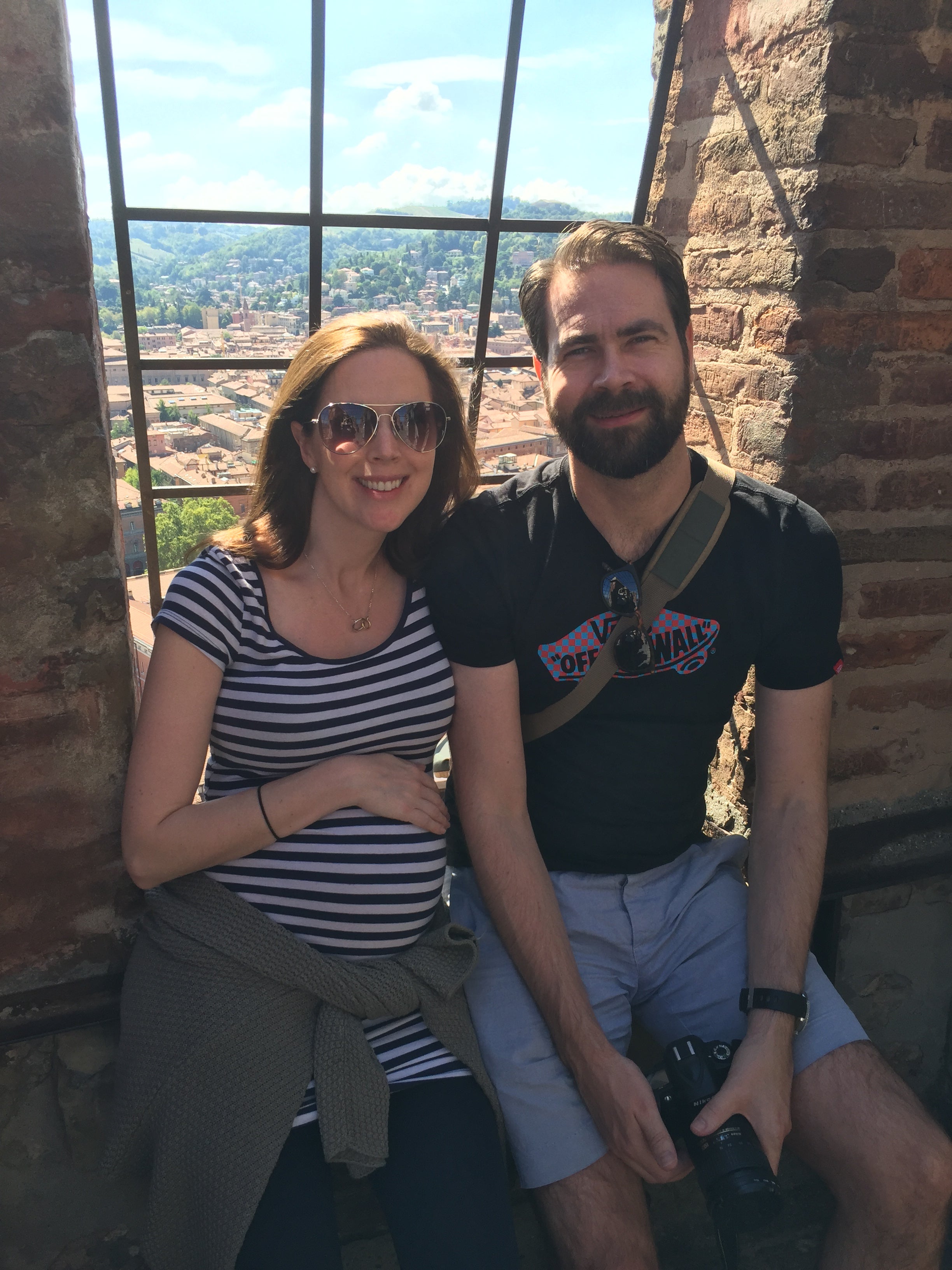Two people standing close together with a scenic view outside a large window.